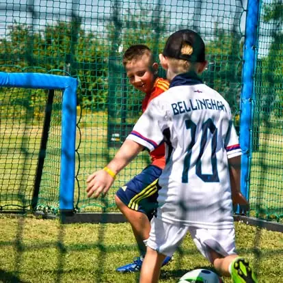 Dzieci grają jeden na jeden w mini boisku z miękkimi zabezpieczeniami bramek - bezpieczna gra na małej przestrzeni.