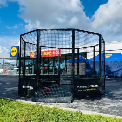 Football Octagon ustawiony na parkingu przed sklepem - szybki montaż mobilnej areny piłkarskiej na czas eventu.