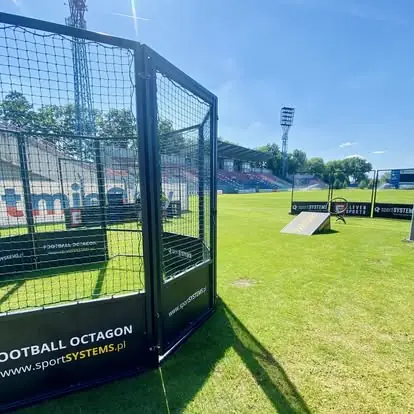Arena Football Octagon i urządzenia treningowe rozstawione na murawie stadionu przed wydarzeniem sportowym.