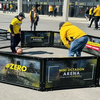 Dorośli i dzieci grają razem w Mini Octagon Arena przed wejściem na stadion.
