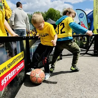 Dzieci walczą o piłkę przy bandzie Mini Octagon Arena w strefie Street Soccer.